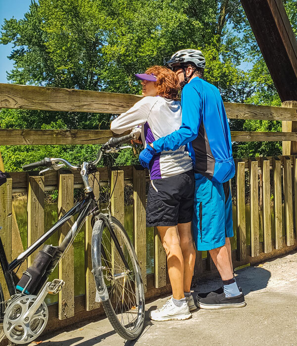 two adults in bicycling gear on a bridge looking at the view