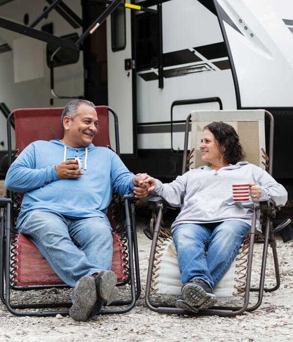 man and woman sitting in camping chairs in front of their camper