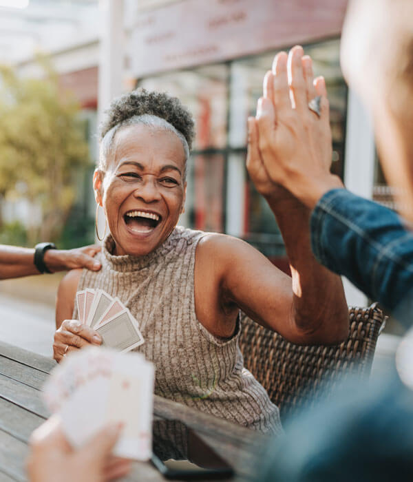 senior woman high-fiving a friend while playing cards outdoors