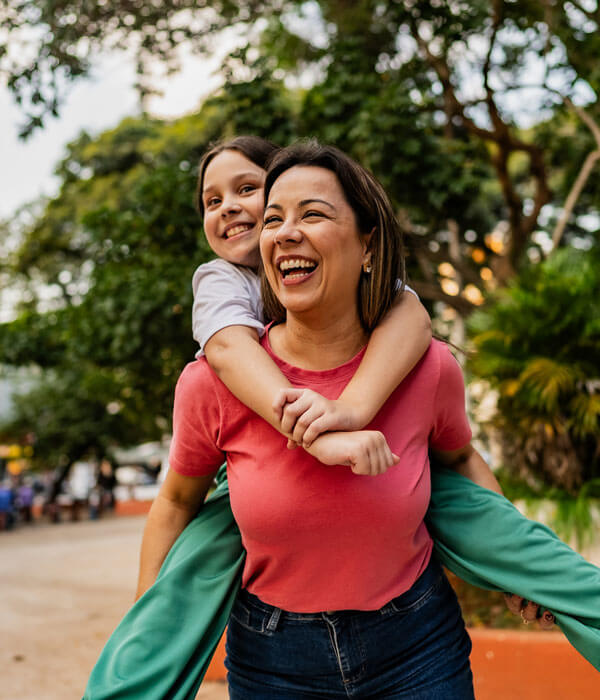 mom giving her daughter a piggy back ride in the park