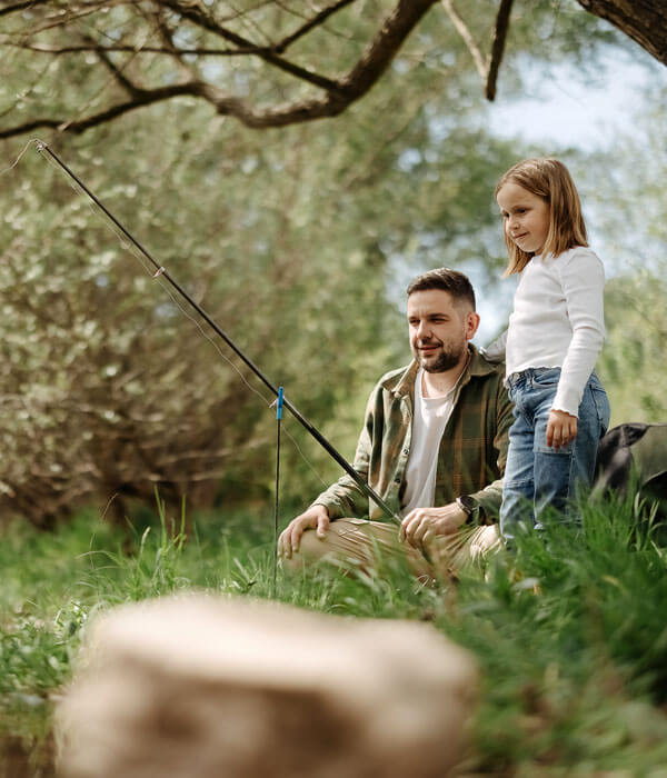 a dad and his daughter fishing on the bank of a pond