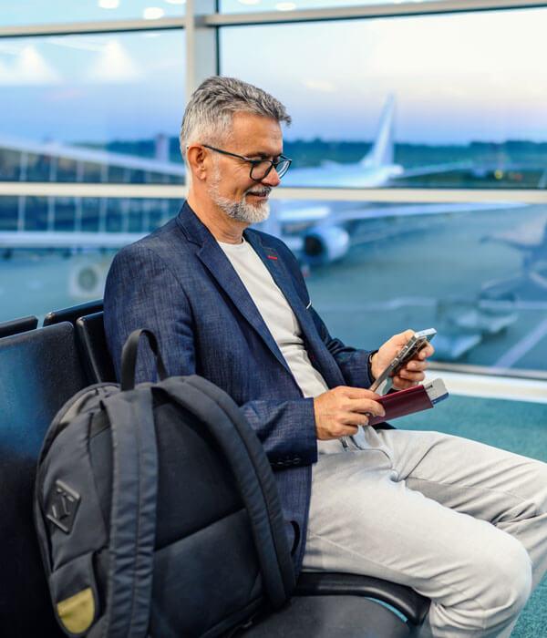 senior man sitting in the airport looking at his phone and smiling